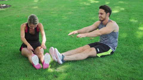 Young couple stretching before fitness workout at green grass in summer park. Sport man together woman doing stretch exercise outdoor at summer. FItness couple stretching