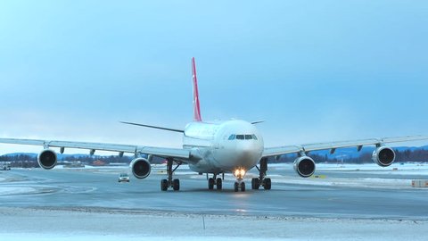 oslo airport norway - ca january 2019: huge airplane turkish airlines a340 taxiing front view winter scenery small folow me car behind