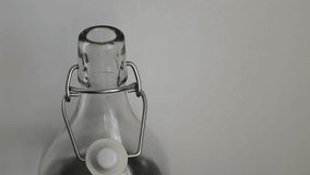 Caucasian man's hand closes the cap of the glass bottle full of water. Neutral white background. 30fps 4K video.