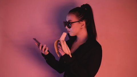 Brunette girl eating a banana. Browse the web page. She is in neon lighting.