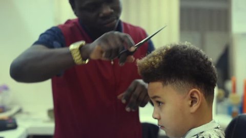 Boy in the african barbershop. Cute mixed boy makes a haircut in the African salon. Hair style. Haircut by scissors for children. School boy hair style. 