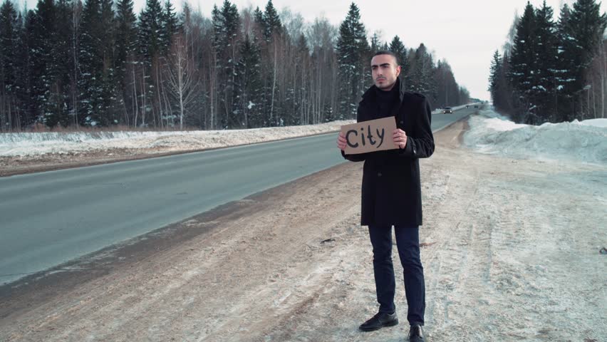 Man hitchhiking at winter country road with cardboard plate. 4k