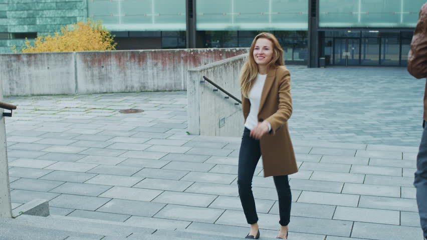 Cheerful and Happy Young Woman Actively Dancing While Walking Up the Stairs. She's Wearing a Long Brown Coat. Scene Shot in an Urban Concrete Park Next to Business Center. Day is Bright. Royalty-Free Stock Footage #1024342478