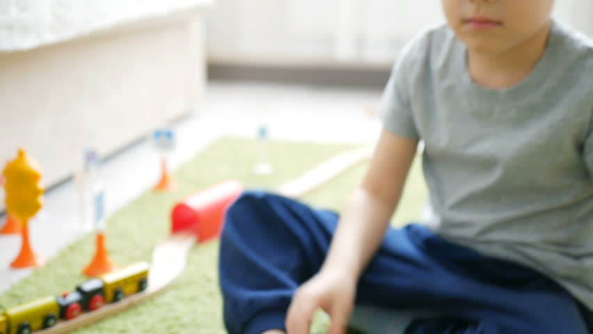 Two years old boy plays with wooden railroad in a sunny room