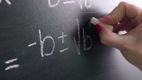 Math teacher writing equation or function on blackboard in school classroom. Student doing exercise on chalkboard in university or college. Woman teaching or studying. Close up with camera movement.