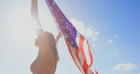 Low angle view of young Caucasian woman holding a American flag on the beach. American flag fluttering in her hands วิดีโอสต็อก