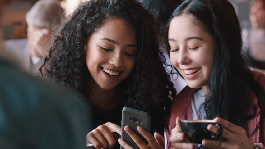Happy teenage girl friends using smartphones drinking coffee in cafe texting hanging out sharing gossip enjoying chatting together | Shutterstock HD Video #1024356218