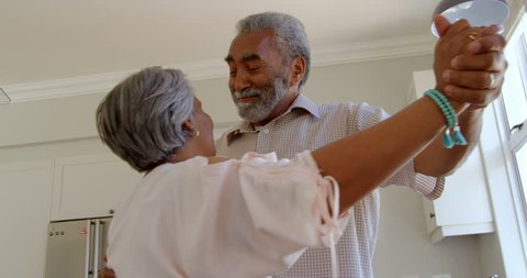 Side view of senior African-american couple dancing together in kitchen at comfortable home. They are smiling and holding hands, Social distancing and self isolation in quarantine lockdown for Covid