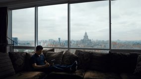 Relaxed man Greets using tablet for a video call. Cheerful smiling caucasian man sitting on couch having a friendly video call. Happy man enjoying video calling on sofa. with beautiful view of Moscow