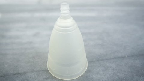 Tampons fall in slow motion on a silicone menstrual cup. The cotton feminine hygiene products drop and bounce by the menstrual cup on the marble counter top.
