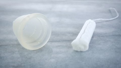 Woman chooses a tampon over a menstrual cup. The girl grabs the string of the cotton feminine hygiene product and drags it out of frame leaving the silicone cup and room for copy space behind.