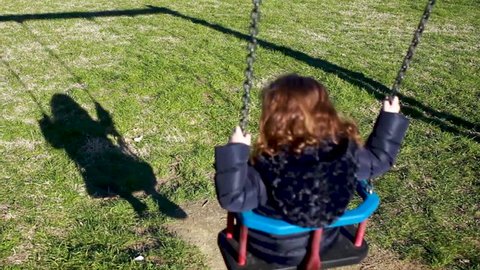 Toddler girl plays on the swing. Science concept, example of shadow, energy, inertia and gravity.