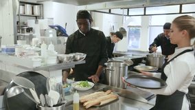 Successful young waitress taking cooked ordered meals from female chef in restaurant kitchen