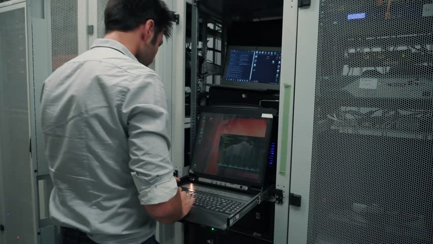 IT Engineer Working On Computers Console In A Server Room. Man Using Console Computer In Server Room Or Data Center. Technical Engineer Working With Laptop Panel To Resolve Problem In Datacenter Room Royalty-Free Stock Footage #1024393964