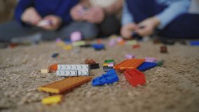 Blocks of constructor with different color and shape are on the carpet on the background of children and adults playing with it. Close-up. Blurred background.