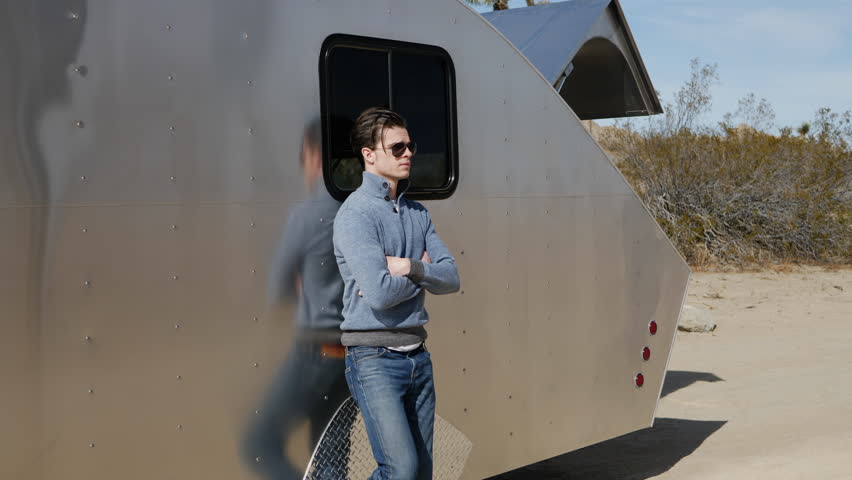 An attractive young man and digital nomad traveling solo in a metal travel trailer tiny house in the California desert. | Shutterstock HD Video #1024399649