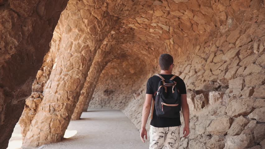 Man tourist is examining beautiful fake grotto in parc. He is strolling inside gallery with columns and touching walls