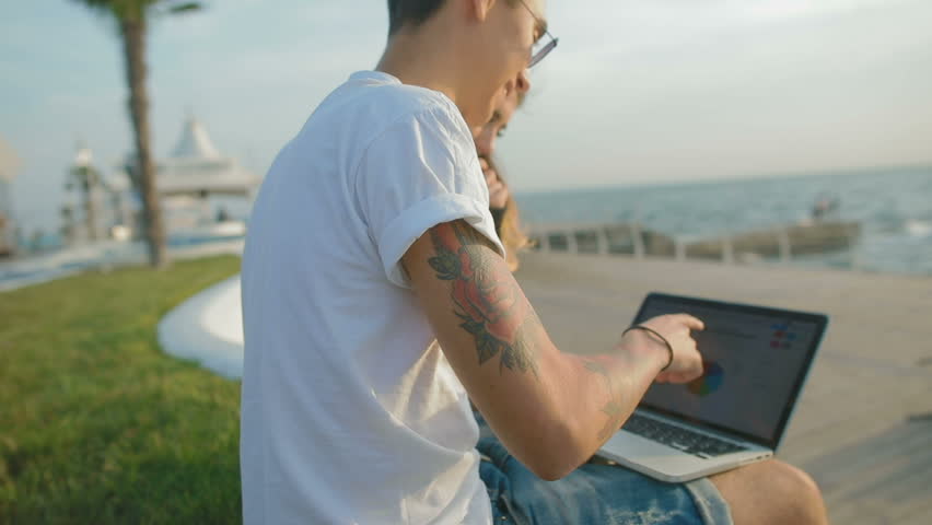slow motion guy in white t-shirt shows and explains girlfriend multicoloured graph with diagram against sea