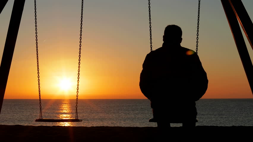 Back view silhouette of a man alone contemplating sunset sitting on a swing on the beach Royalty-Free Stock Footage #1024406963