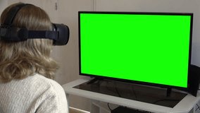 Virtual Reality Headset Girl Watching TV Green Screen Television. Young woman wearing a virtual reality headset in front of a green screen television.