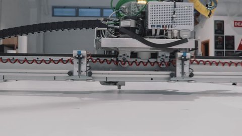 A robotic arm,ing while processing a large scale panel. Details from a big, professional, CNC printer. Motion blur, highlighting the advances and progress in the engineering and technology fields.