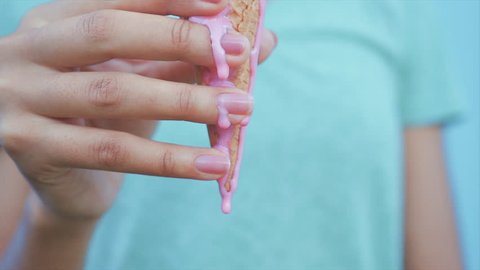young afro girl eating pink melting ice cream at blue wall background