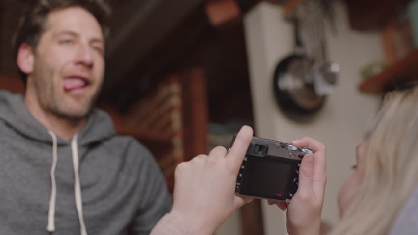 happy young couple taking photos together using camera having fun at home on sofa playfully enjoying romantic relationship photographing each other making faces