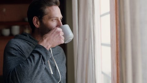 young man opening curtains looking out window enjoying fresh new day feeling rested drinking coffee at home