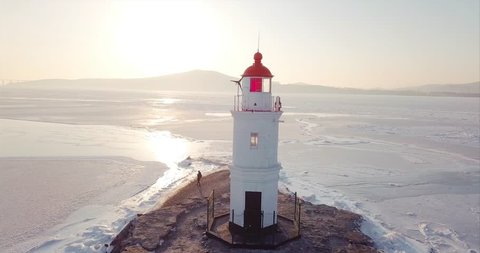 Aerial panoramic view of a lighthouse perched on a rocky Tokarevsky Spit. It's one of Vladivostok’s main attractions. Russian Bridge across frozen Eastern Bosphorus strait is on the background.