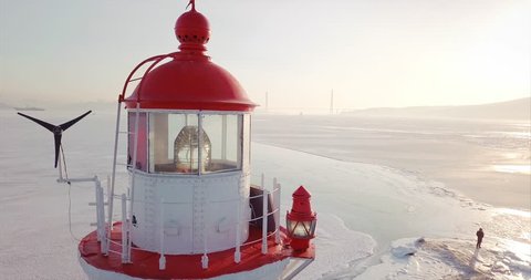 Close aerial view of a lighthouse perched on a rocky Tokarevsky Spit. It's one of Vladivostok’s main attractions. Russian Bridge across frozen Eastern Bosphorus strait is on the background. Morning