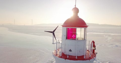 Close aerial panoramic view of a lighthouse perched on a rocky Tokarevsky Spit. It's one of Vladivostok’s main attractions. Russian Bridge across frozen Eastern Bosphorus strait is on the background.