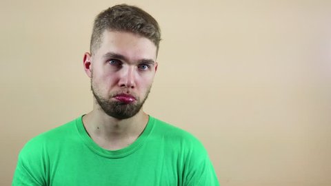 Portrait of a guy in a green t-shirt posing with a sad look, over a beige background. Concept of emotion