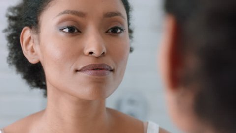 portrait beautiful african american woman looking in mirror at perfect skin enjoying natural complexion getting ready at home