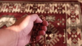 Close up view of a Muslim man hand counting prayer beads or tasbih on a prayer mat. Selective focus.