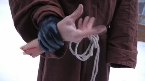 Horror hand. Man in monk outfit hold severed joke hand and wiggles fingers. Handheld shot with stabilized camera.