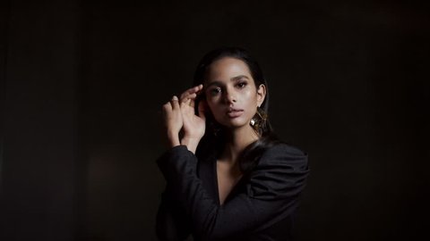 Portrait Of A Seductive Young Woman On A Dark Background. Black Shiny Blouse With A Deep Neckline.