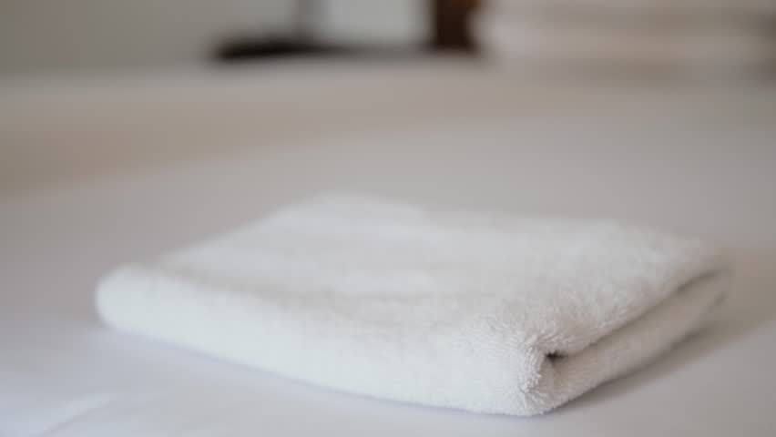Close-up of hands putting stack of fresh white bath towels on the bed sheet. Room service maid cleaning hotel room macro closeup | Shutterstock HD Video #1024445465
