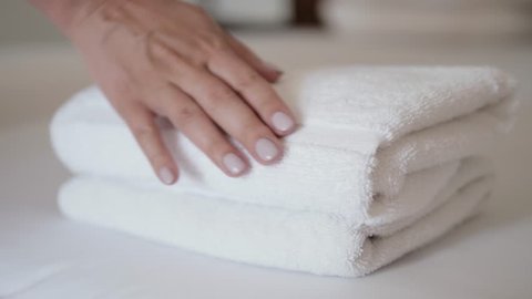 Close-up of hands putting stack of fresh white bath towels on the bed sheet. Room service maid cleaning hotel room macro closeup