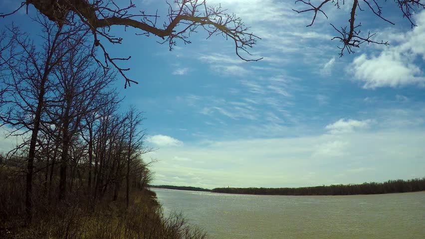 Early spring riverside moving timelapse of two levels of clouds on sunny day with trees and branches at riverside. Selkirk Red River Manitoba Canada