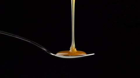Honey pours onto a spoon and drips over the edges
