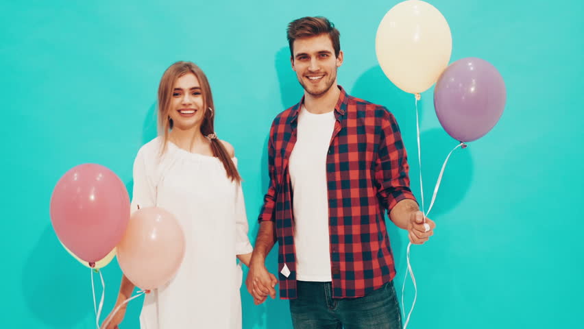 Portrait of Smiling Beautiful Girl and her Handsome Boyfriend holding bunch of colorful air balloons and laughing. Happy Valentine