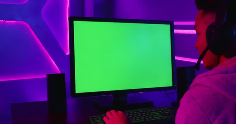 Young Asian Pro Gamer Playing in Online Video Game with green chroma key screen computer
