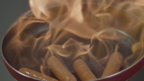delicious sausages on a hot pan with fire in slow motion