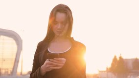 Close-up of young professional businesswoman using smartphone and drinking coffee to go outdoors, sunlight, slow motion