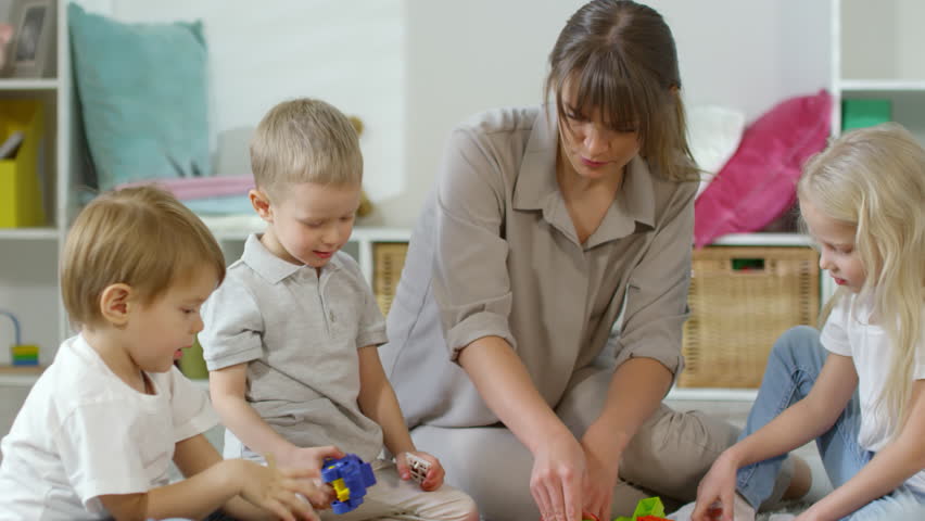 Sequence of videos of female teacher and group of preschool kids playing with construction set on the floor in kindergarten, boy connecting colorful blocks and girl making toy house Royalty-Free Stock Footage #1024459937