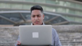 Sad young man looking at laptop and rubbing face. Upset middle eastern businessman reading bad news and closing laptop outdoor. Bad news concept