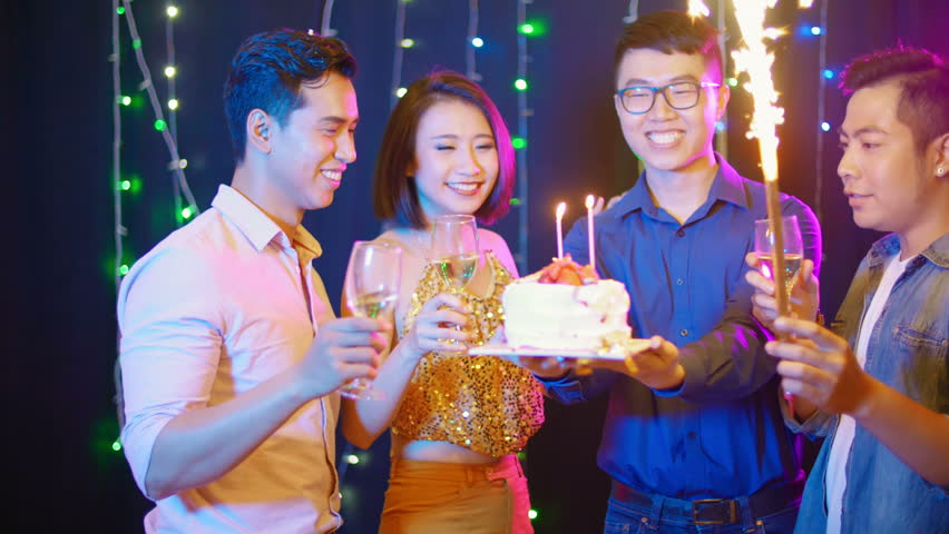 Lockdown of several friends cheering with champagne on bday party of their male friend who holding cake
