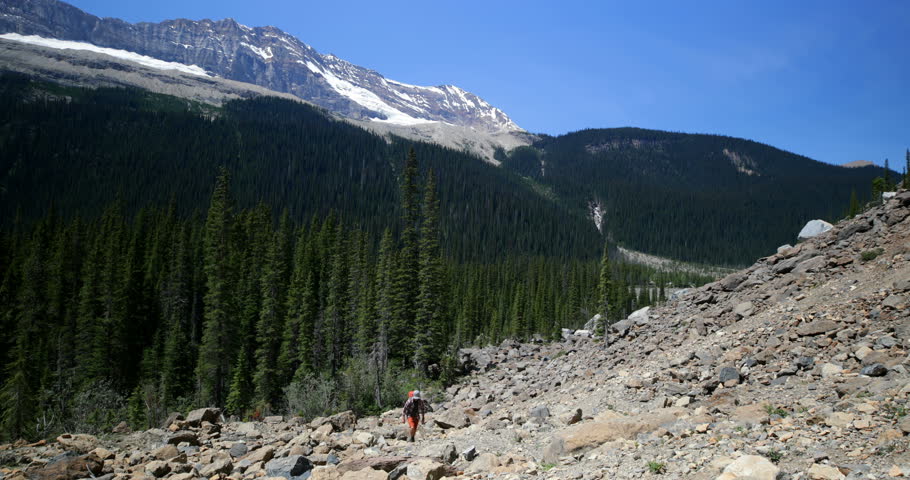 Front view of young caucasian male hiker with backpack hiking on mountain. He is walking in the sunshine 4k