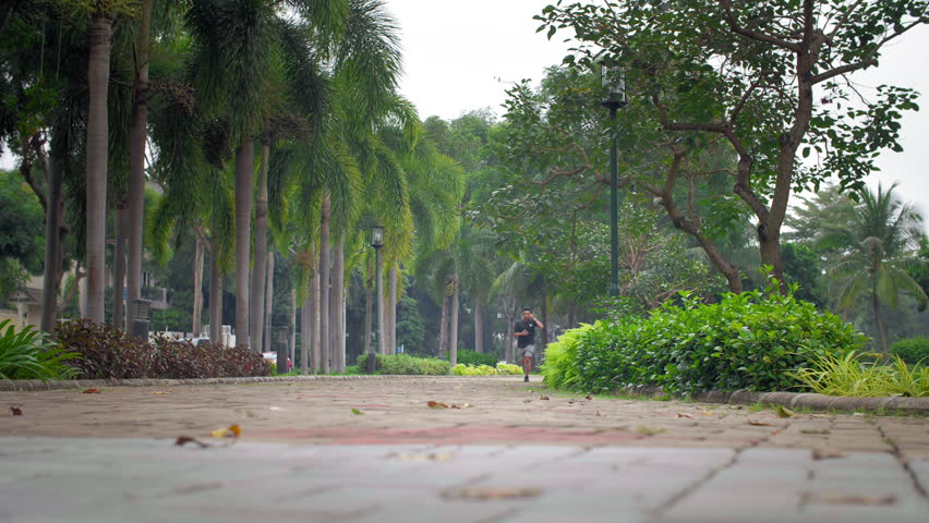 Wide shot of sporty Asian man jogging in park