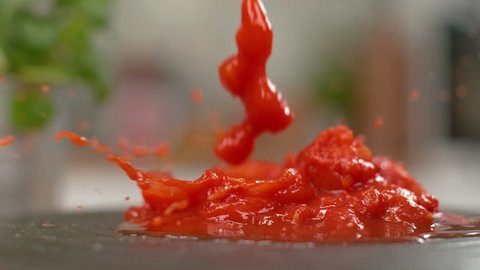 MACRO, DOF, SLOW MOTION: Tasty pieces of raw tomato fall into the fresh marinara sauce. Cherry tomato chunks falling into the homemade puree served on a black plate. Delicious vegetarian pasta sauce
